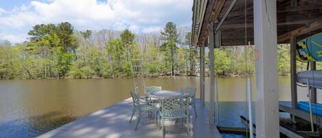 A wooden deck with a table and chairs overlooking a calm lake, surrounded by trees.