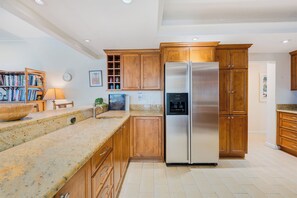 A kitchen with wooden cabinets, a stainless steel refrigerator, a granite countertop, and a built-in oven.