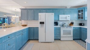 A modern kitchen with blue cabinets, a white refrigerator, a microwave, and a stove.