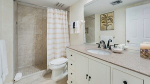 A bathroom with a shower, toilet, sink, and a large mirror.