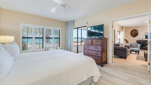 A hotel room with a large bed, a dresser, a TV, and a view of the beach.