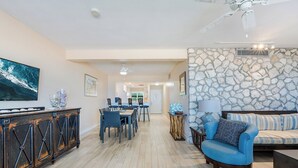 A spacious living area with a dining table, blue chairs, a sofa, and a stone accent wall.