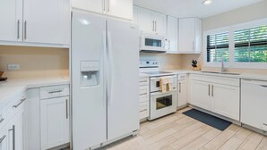 A modern kitchen with white cabinetry, a built-in water dispenser, a microwave, an oven, and a window with blinds.