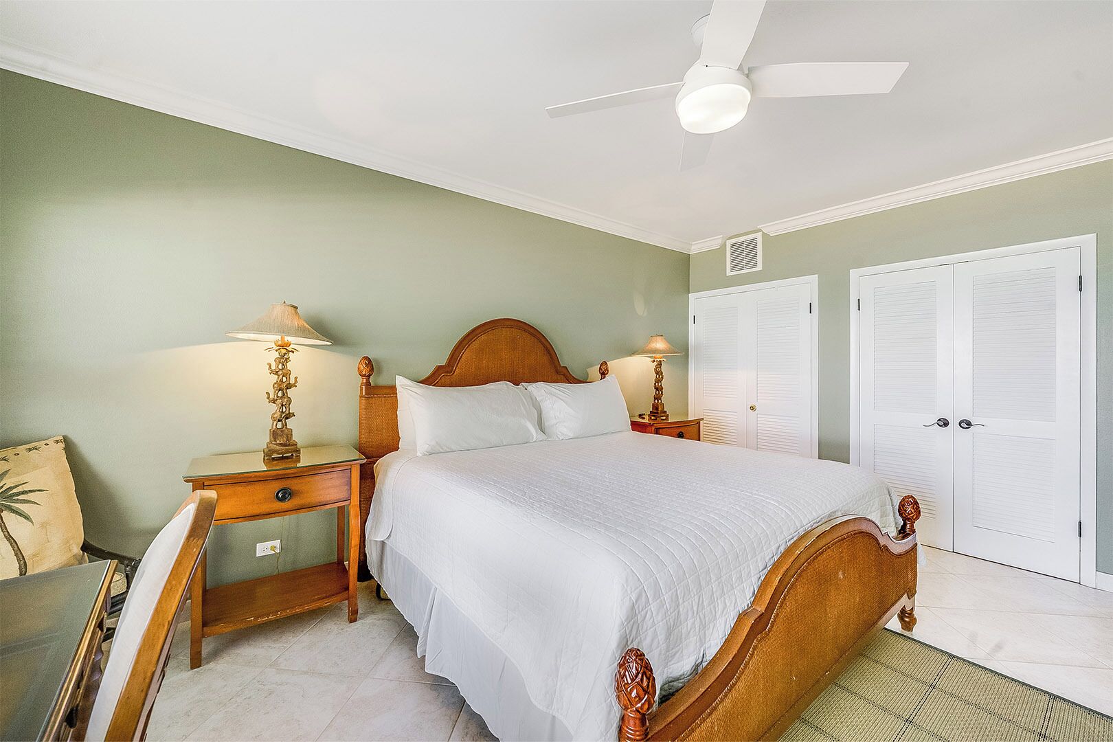 Une chambre à coucher comprenant un lit, des tables de chevet, un ventilateur de plafond et une armoire.