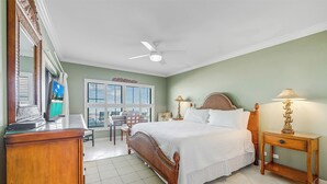 Una camera da letto con un letto, comodini, una scrivania, una sedia, una televisione e una ventola a soffitto.