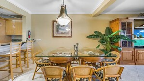 Un'area pranzo con un tavolo in vetro, sedie in vimini, una lampada a sospensione e una pianta grande.