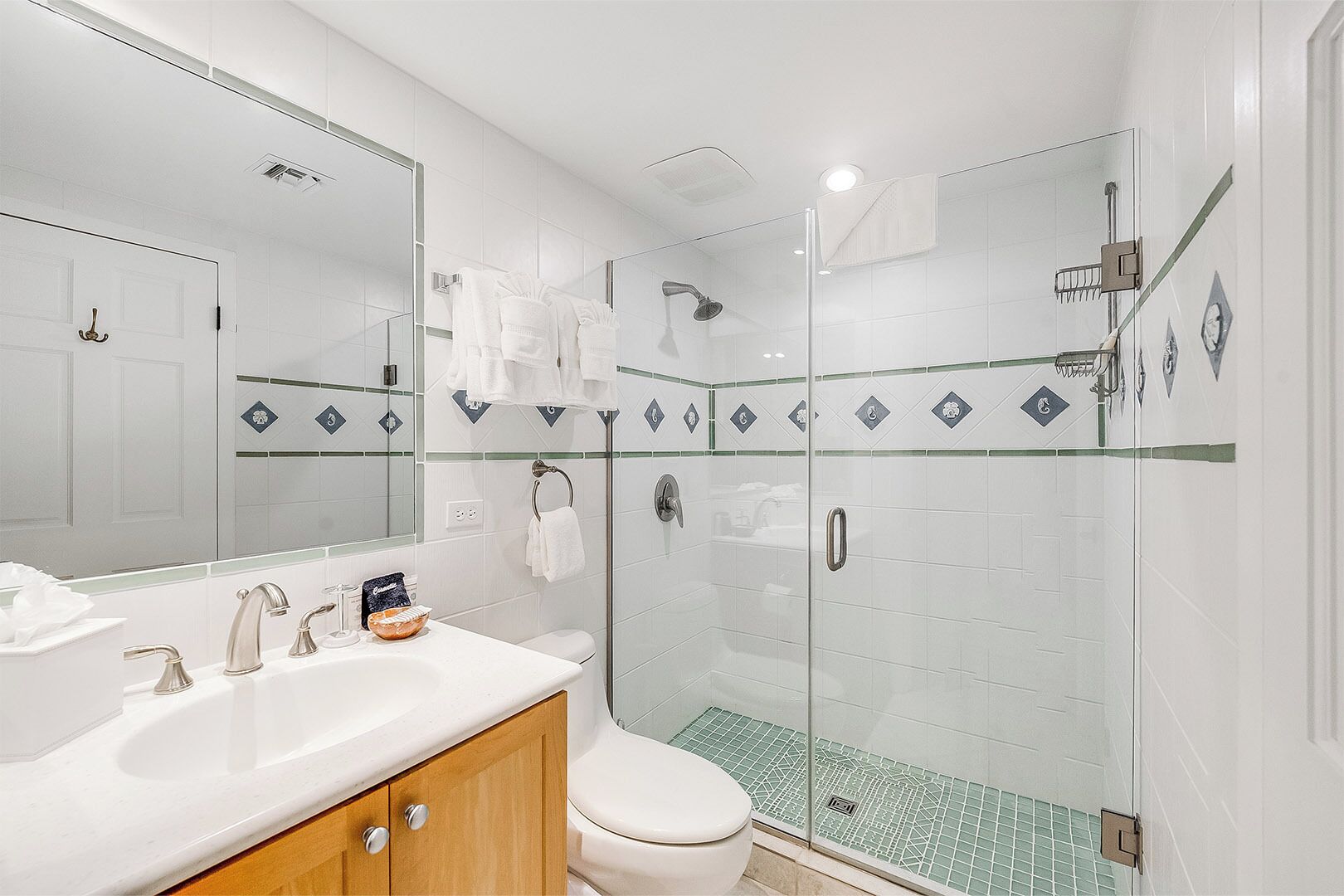 Un baño moderno con ducha envuelta en cristal, un lavabo blanco con espejo y un inodoro.
