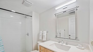 A modern bathroom with a shower, toilet, vanity with a mirror, and a sink. - Casa Caribe #11 - 3 Bed, 3 Bath - Oceanfront, Second Floor (Seven Mile Beach)