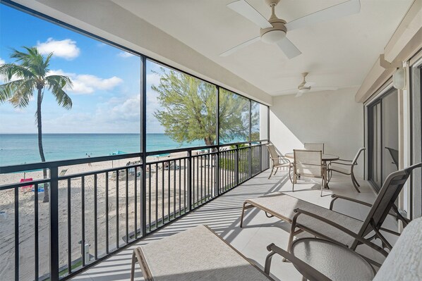 A balcony with a view of the beach and ocean, equipped with chairs and a table.
