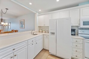 A modern kitchen with white cabinetry, a stainless steel sink, a refrigerator, and a microwave.