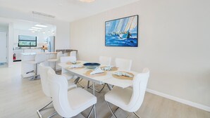 Un comedor moderno con una mesa blanca, sillas y un cuadro de veleros.