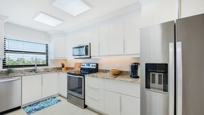 Una cocina moderna con electrodomésticos de acero inoxidable, armarios blancos y una ventana con persianas.