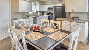 Een moderne keuken met witte kastjes, een donker houten eettafel en een kroonluchter.