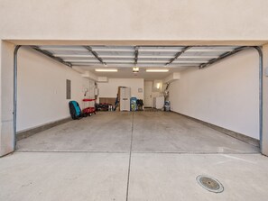 Un garaje con piso de concreto, una puerta blanca e iluminación fluorescente en el techo.