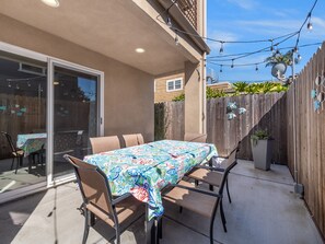 An outdoor patio with a table and chairs, a sliding glass door, and a wooden fence. - Pacific Beach Dreamin' - AC, Garage, Walk to Beach & Town (San Diego)