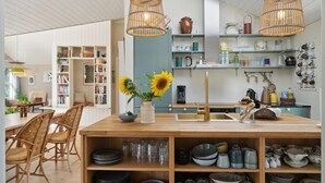 A modern kitchen with wooden shelves, a central island, and a dining area with wicker chairs. - 3 bedroom stunning home in Rødby (Rødby)