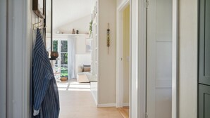 A hallway with a wooden floor, a hanging coat rack, and a door leading to a room with a bed and a window. - 3 bedroom stunning home in Rødby (Rødby)