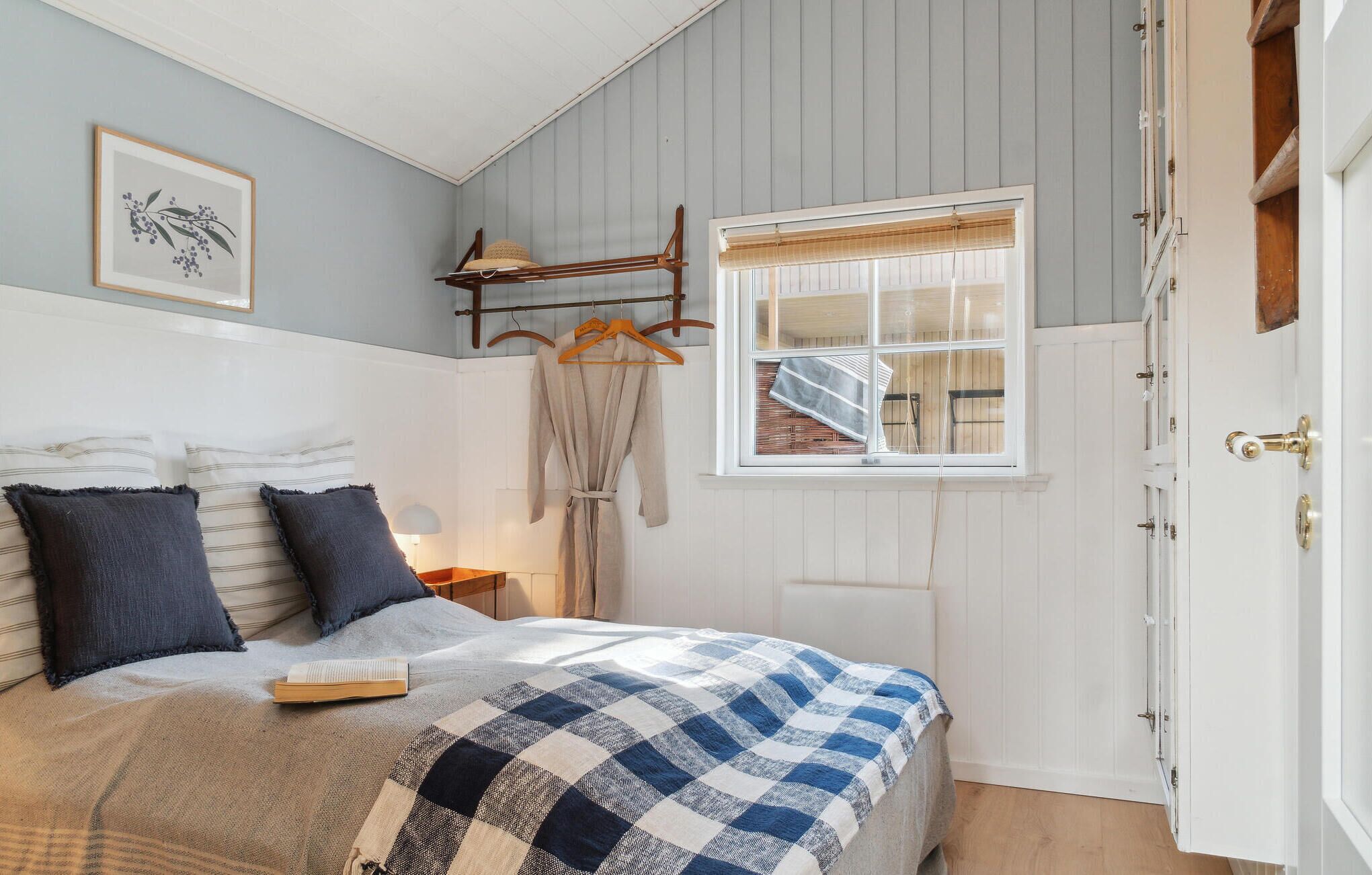 A bedroom with a bed, a window with blinds, a wooden coat rack, and a door.