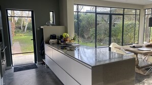 A modern kitchen with a large island, a dining area with a table and chairs, and large windows offering a view of the garden.