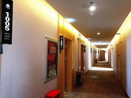 Pasillo de hotel con puertas numeradas, un carretel de manguera contra incendios y un banco rojo.