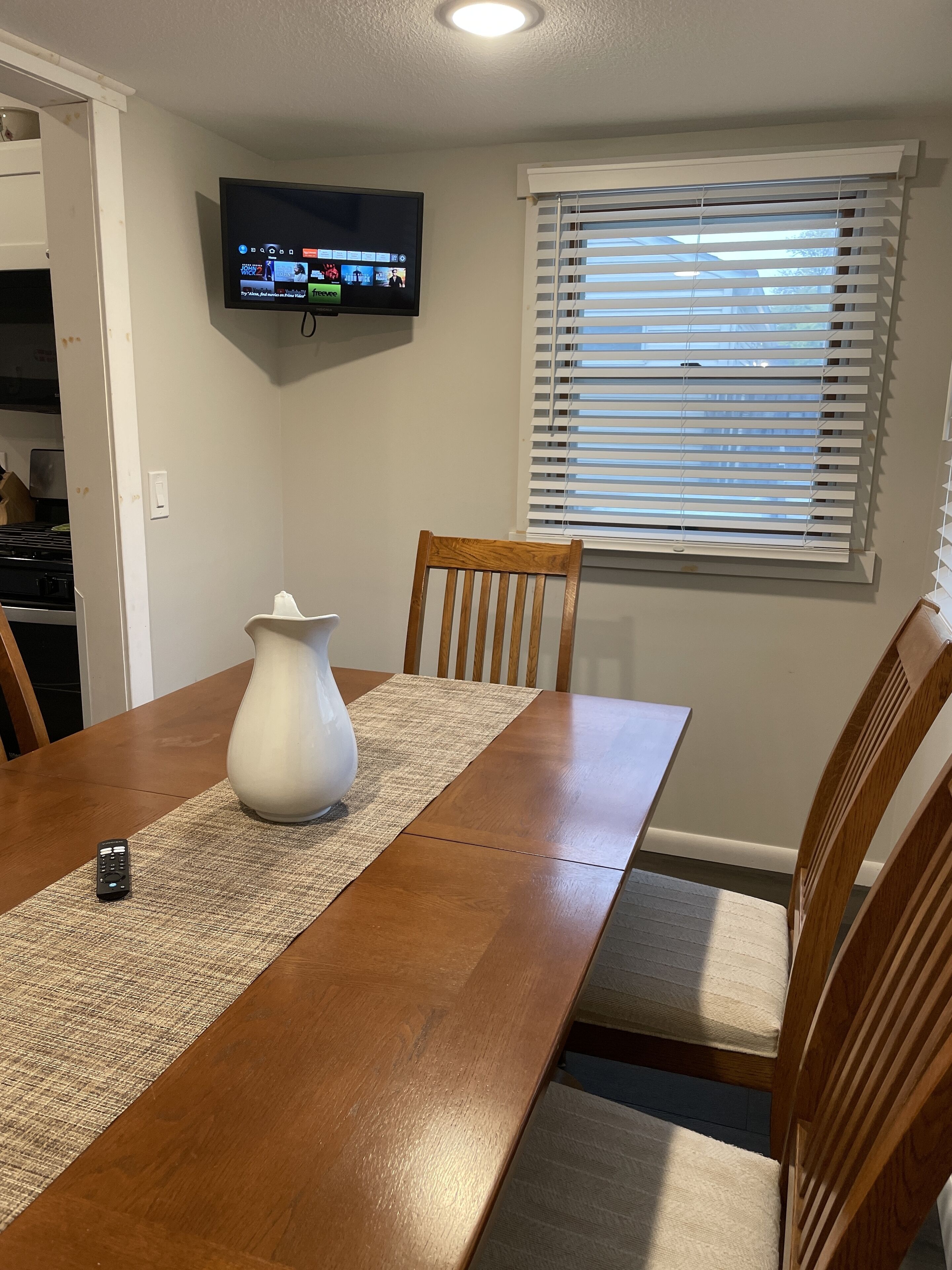 Una sala da pranzo con un tavolo di legno, sedie, un vaso e una televisione montata a parete.
