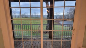 A view through a window with a grid pattern, overlooking a wooden deck and a grassy area with trees in the background. - Lakehouse Vineyard on Lake Erie! (Ripley)