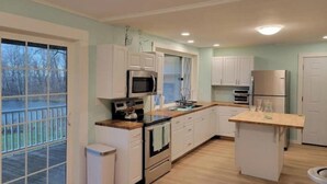 A modern kitchen with white cabinets, stainless steel appliances, and a large window overlooking a deck. - Lakehouse Vineyard on Lake Erie! (Ripley)