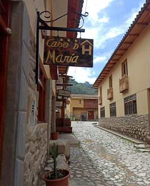 Eine enge Kopfsteinpflasterstraße mit einem Schild für 'Casa de María', das an einem Gebäude hängt.