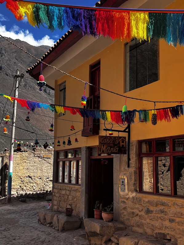 A building with a stone facade, a sign reading "Casa de María", and colorful decorations hanging above the entrance. - Casa D Maria (Ollantaytambo)