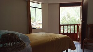 A bedroom with a bed, a chair, and a balcony with a view of greenery. - Casa D Maria (Ollantaytambo)