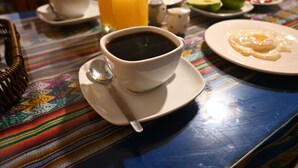 A table with a cup of black coffee, a glass of orange juice, and plates with food. - Casa D Maria (Ollantaytambo)