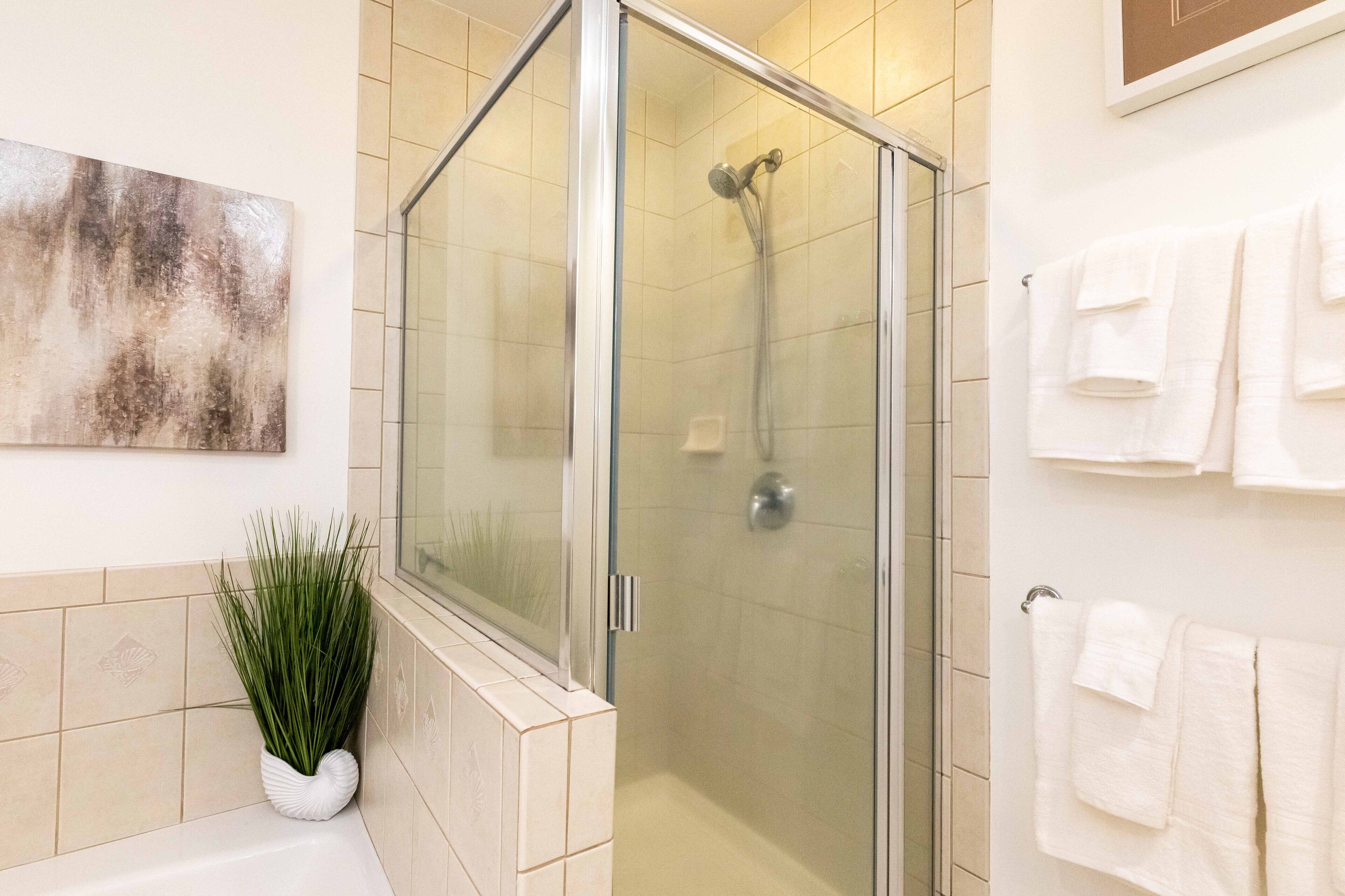 Un baño moderno con ducha de vidrio, una bañera blanca y una planta en maceta.