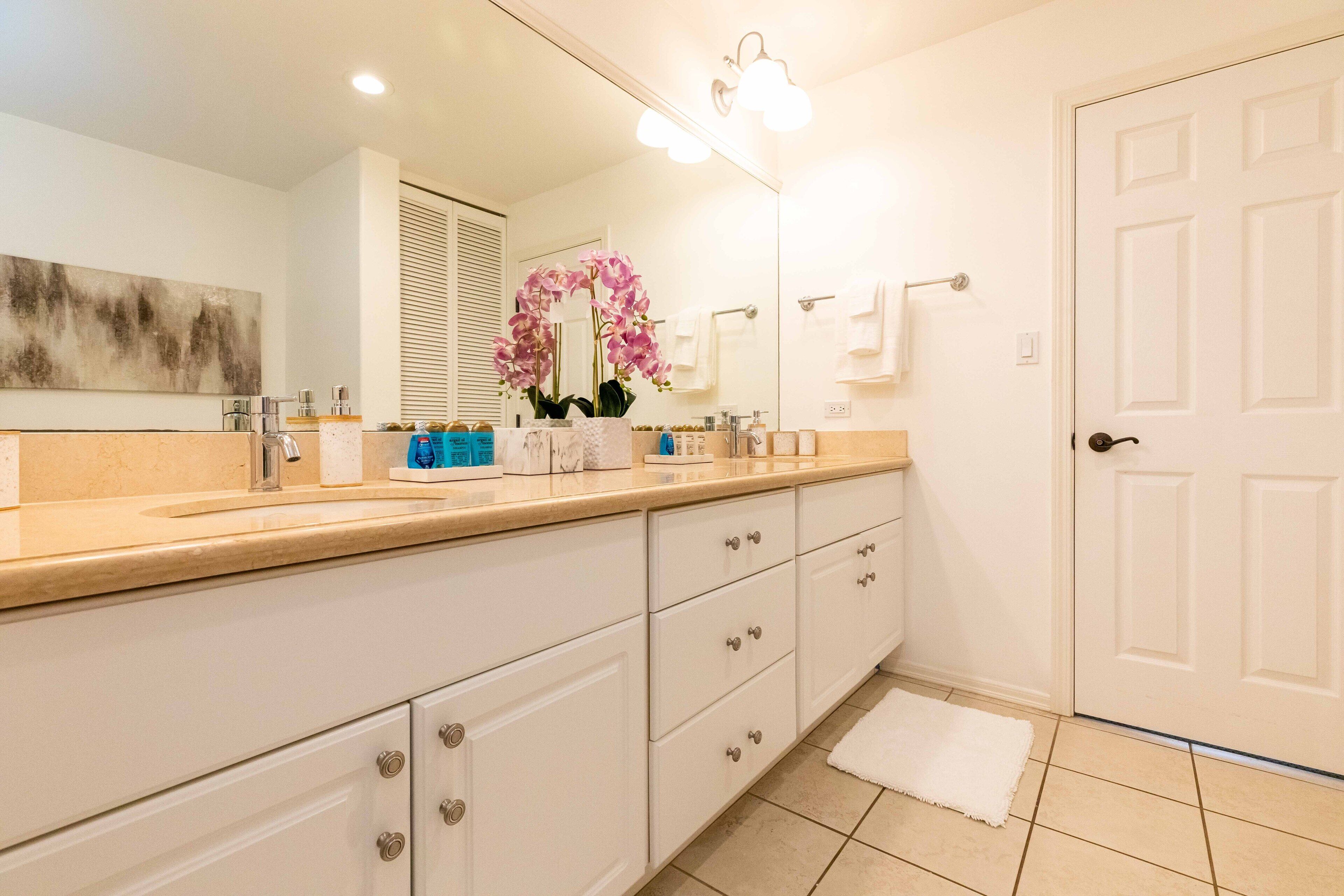 A modern bathroom with a large mirror, two sinks, a towel rack, and a door.