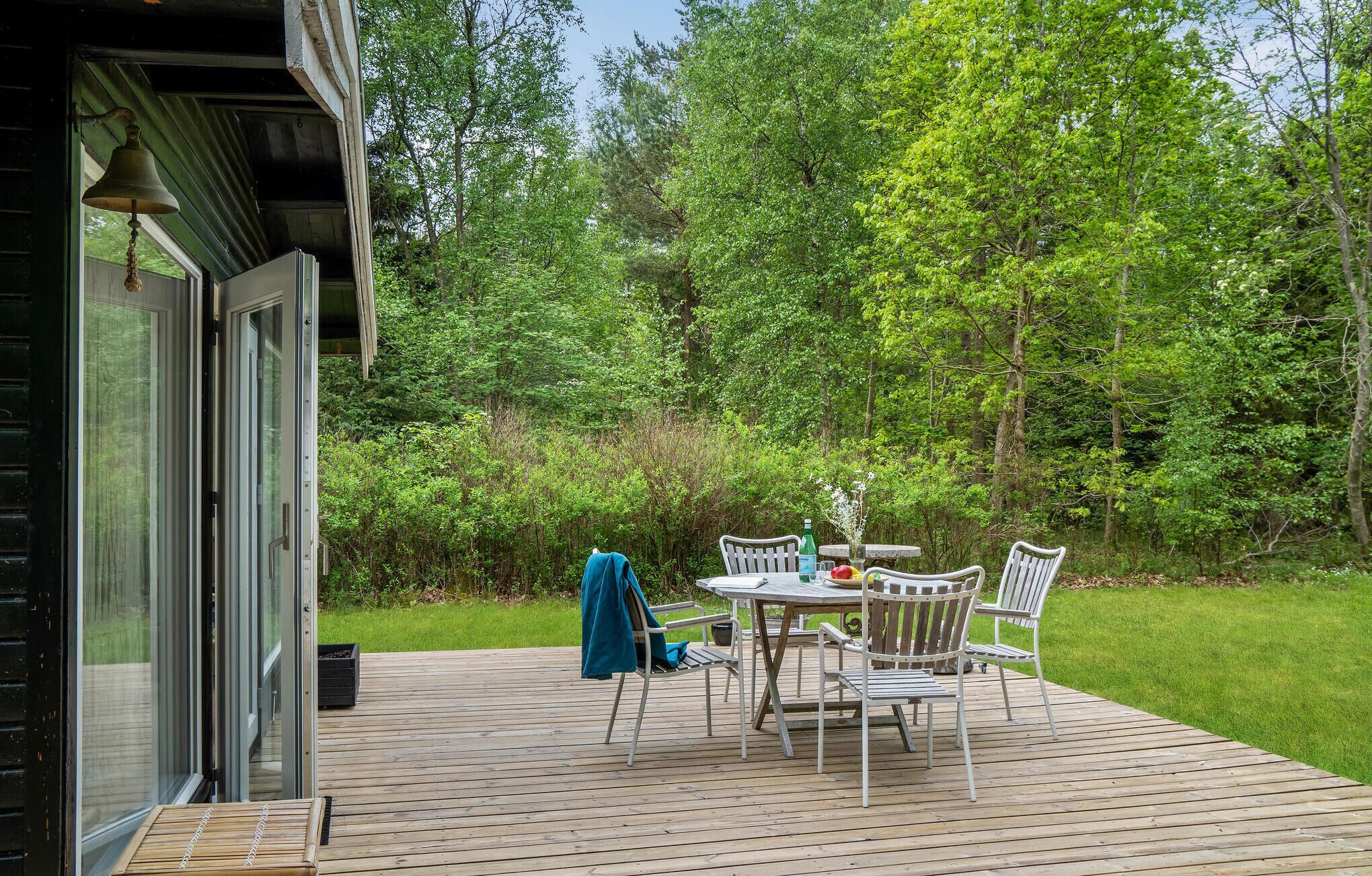 A wooden deck with a table and chairs, surrounded by lush greenery and trees.