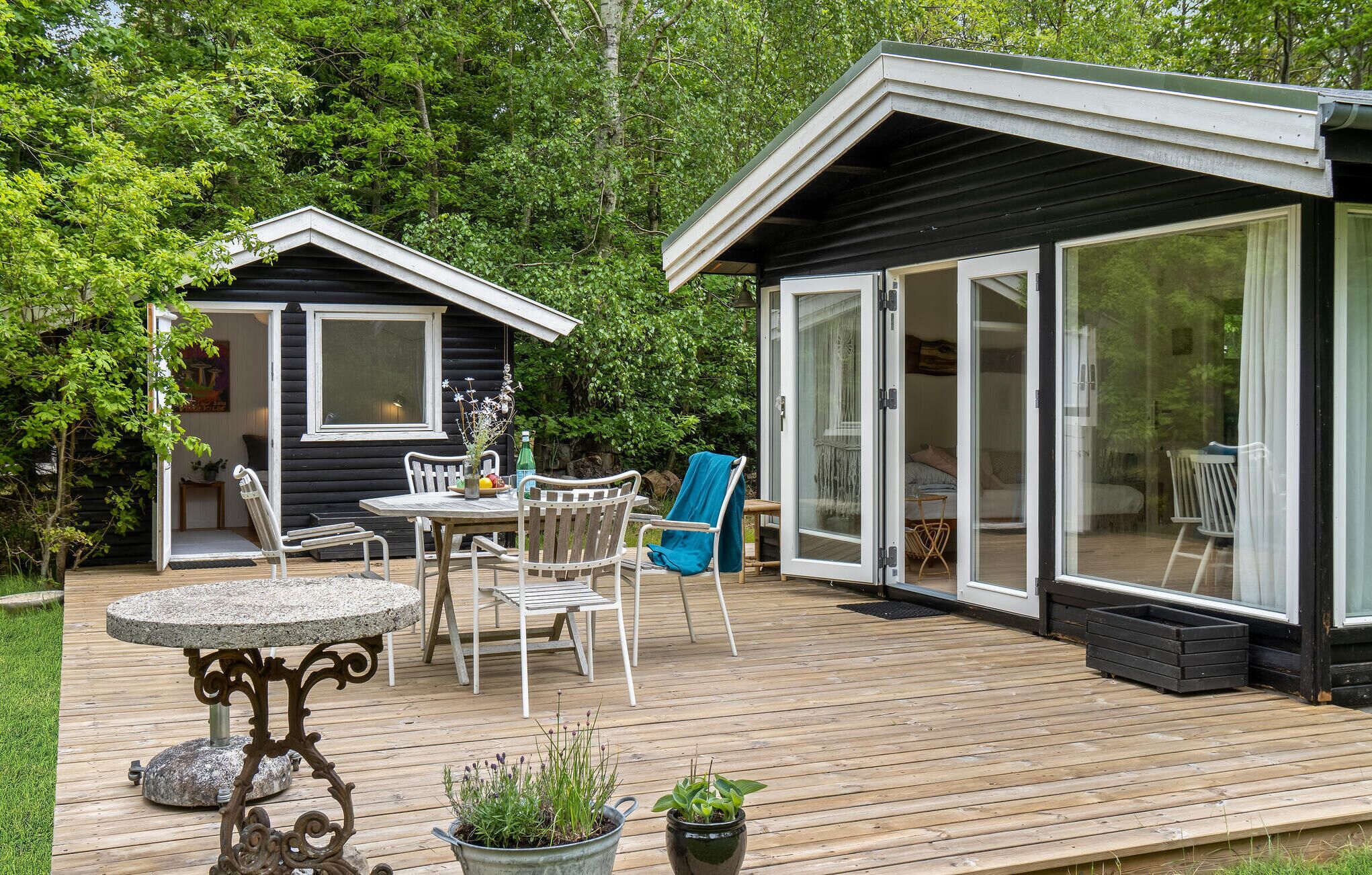 Een houten terras met een stenen tafel, witte stoelen en potplanten.