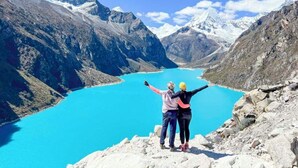 Un couple se tient sur un promontoire rocheux, surplombant un lac turquoise avec des montagnes en arrière-plan.