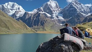 Un groupe de personnes est assis sur un rocher au bord d’un lac, avec une chaîne de montagnes en arrière-plan.