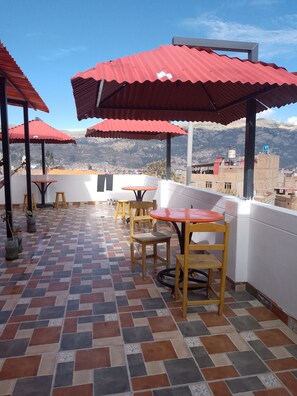 Une terrasse agrémentée de parasols rouges, dotée d’un sol carrelé et de mobilier en bois.