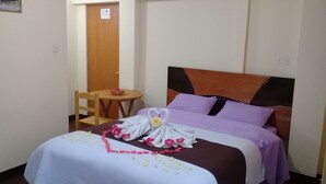 Une chambre d’hôtel avec un lit, une chaise en bois, une petite table ronde et une porte.