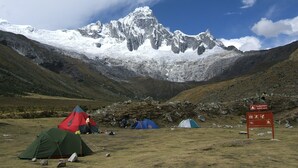 Un paysage montagneux avec des tentes et un panneau indiquant un sentier.