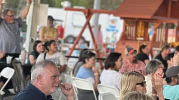 A crowded outdoor event with people seated at tables, some holding drinks.