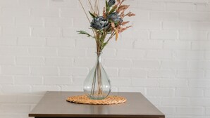 A table with a vase of flowers and a placemat, set against a white brick wall. - Whitney Ridge Resort (Clifton)