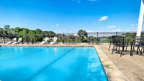 A rectangular swimming pool with clear blue water, surrounded by a black metal fence. There are several lounge chairs and a table with chairs on the right side of the pool. - Whitney Ridge Resort (Clifton)