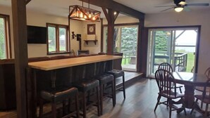 A bar area with a wooden counter and stools, large windows, and a view of the outdoors.