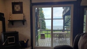A cozy room with a fireplace, a sliding glass door leading to a deck with outdoor furniture, and a view of the ocean.