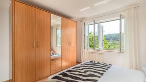 Ein Schlafzimmer mit großem Kleiderschrank, einer Bettdecke mit ZEBRA-MUSTER und einem Fenster mit Blick auf Grünflächen.