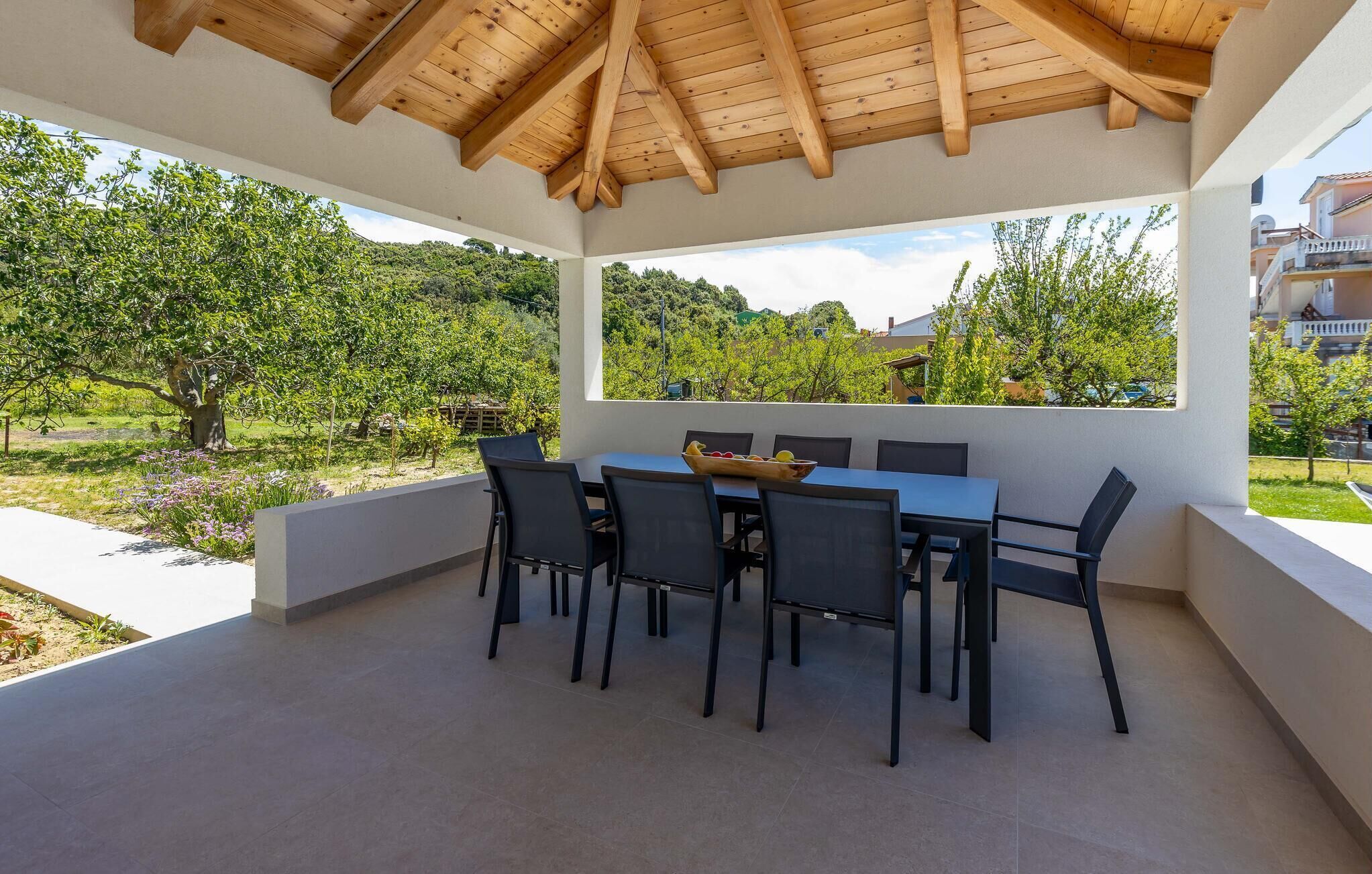 Un espace extérieur abrité, aménagé pour les repas, avec une table et des chaises, un plafond en bois et une vue sur un paysage verdoyant.