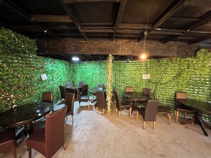 Une pièce aménagée avec des tables et des chaises pour les repas, entourée de murs couverts de verdure et dotée d’un sol en béton.