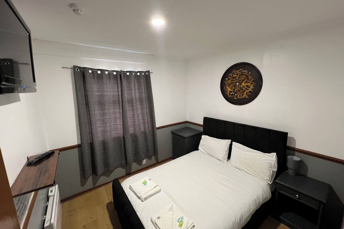 Quarto de hotel com cama, mesas de cabeceira, televisão de tela plana, obra de arte na parede e janela com cortinas.
