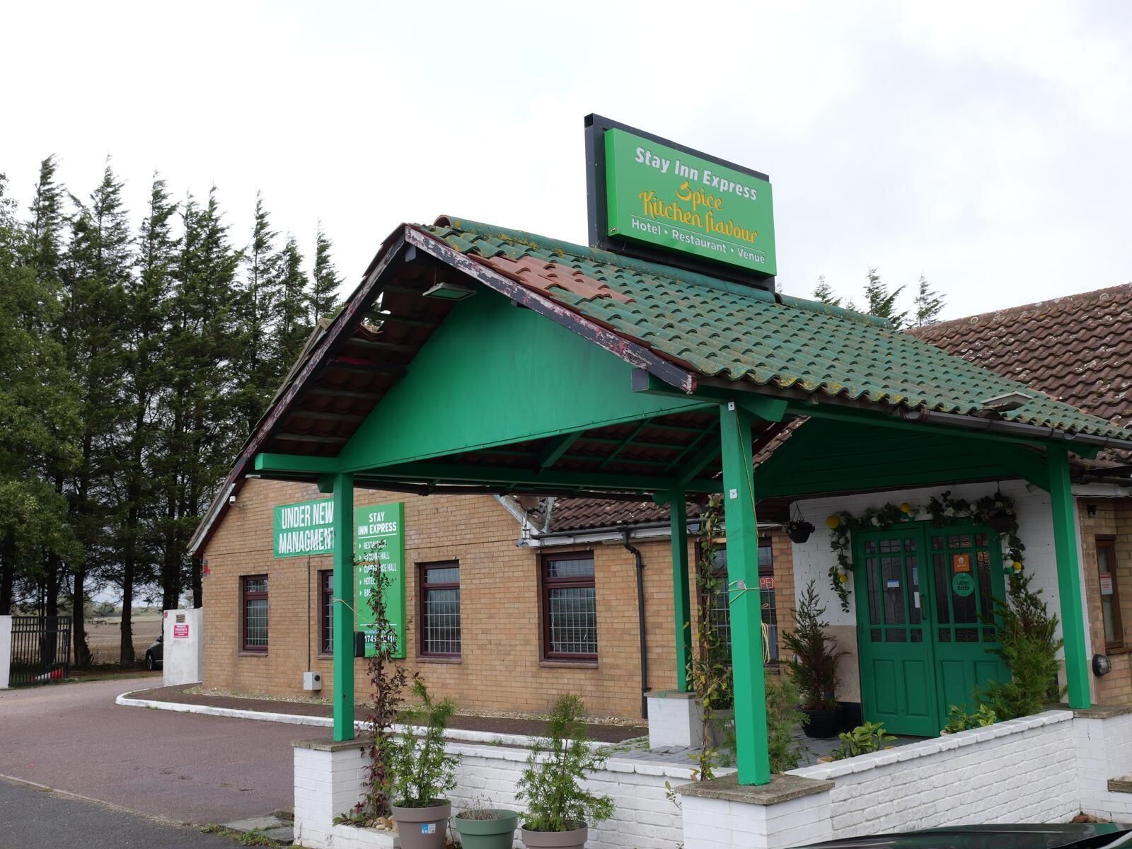 A Stay Inn Express building with a green roof and signage indicating it is under new management.